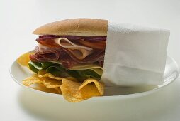 Salami, ham, cheese and salad sandwich in napkin with crisps