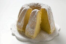 Ring cake with icing sugar, a piece cut, on doily