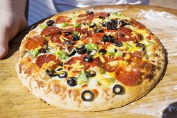 Hands holding pepperoni pizza with peppers and olives