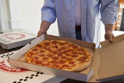 Mann hält Pizzakarton mit Peperoniwurst-Pizza