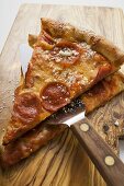 Zwei Stücke Peperoniwurst-Pizza mit Heber auf Holzbrett