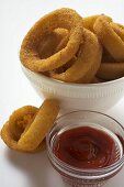 Deep-fried onion rings in white bowl, ketchup