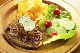 Steak with herb butter on bread, potato crisps and salad