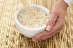 Woman’s hand holding a bowl of rice firmly on a bast cover