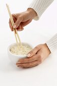 Woman’s hands holding chopsticks in a bowl of rice