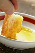 Hand taucht Stück Weißbrot in ein Schälchen Olivenöl