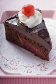 A piece of chocolate cake with cream and glacé cherry