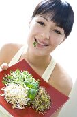Woman with cress in her mouth holding plate of sprouts & herbs