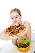 Junge Frau hält Pizza auf Pizzabrett