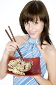 Junge Frau hält asiatisches Nudelgericht mit Essstäbchen