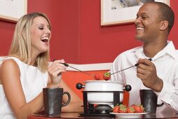 Young woman & man eating chocolate fondue with strawberries