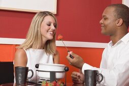 Young woman & man eating chocolate fondue with strawberries