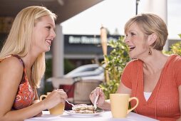 Two women at a street café sharing a piece of tiramisu
