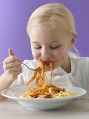 A little blonde girl eating spaghetti with tomato sauce