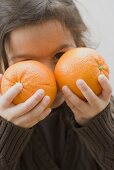 Mädchen hält zwei Orangen vors Gesicht