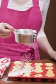 Young woman sprinkling icing sugar over fresh baking