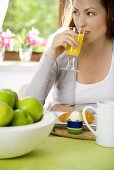 Junge Frau trinkt Orangensaft am Frühstückstisch