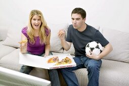 Junges Paar sitzt mit Pizza und Fussball vor dem Fernseher
