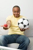Young man with apple and football watching TV