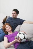 Young couple on sofa with football and bottle of beer