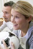 Young couple watching TV with football and pizza