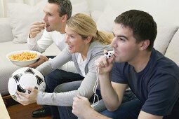 Freunde mit Trillerpfeife, Fussball und Chips beim Fernsehen