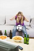 Junge Frau mit Fussball, Bierflaschen & Chips beim Fernsehen