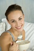 Young woman in bed, eating natural yoghurt