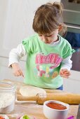 Small girl dusting pizza dough with flour