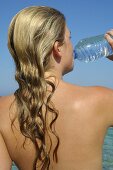 Frau trinkt Wasser aus einer Flasche am Meer