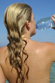 Woman drinking water out of a bottle by the sea