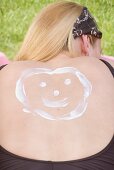 Woman with a face drawn in suncream on her back