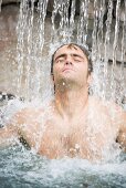 Young man standing under a waterfall