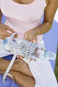 Junge Frau hält Wasserflasche mit Massband