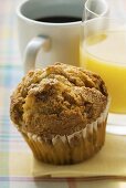 Muffin, dahinter Orangensaft und Kaffee