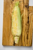 A corn cob with husks on a wooden board