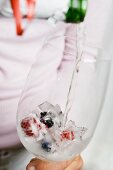 Pouring champagne onto berry ice cubes in glass