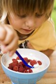 Small child eating yoghurt with fresh raspberries