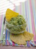 Guacamole in a small glass bowl with nachos