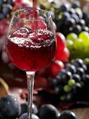 Ein Glas Rotwein eingießen mit Trauben im Hintergrund