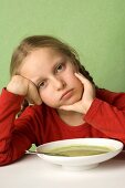 Girl sitting listlessly in front of plate of vegetable soup