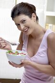 Woman eating yoghurt with kiwi fruit and strawberries