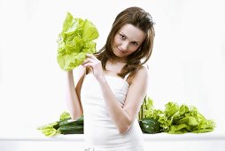 Young woman holding lettuce in her hand, green vegetables behind