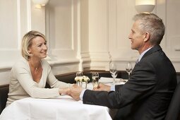 Married couple sitting at restaurant table holding hands