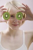 Young woman with two kiwi fruit halves in front of her face