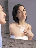 Woman in front of mirror putting cream on her chest