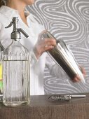 Woman mixing drink in cocktail shaker, soda syphon, bar strainer