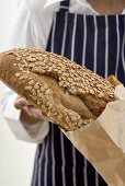 Woman putting a loaf of oat bread into a paper bag