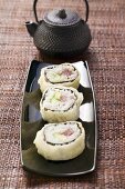 Maki sushi with tuna, cucumber and avocado in front of teapot