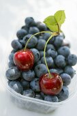 Blueberries and two cherries in plastic punnet